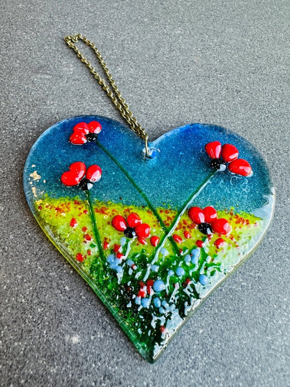 Heart-shaped decorative item with red flowers and a chain on a gray surface