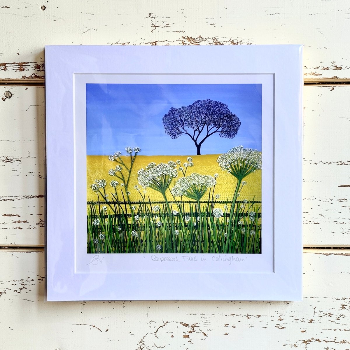 Framed artwork of a tree and flowers on a wooden surface