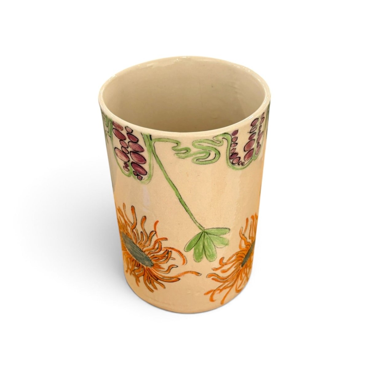 A beige ceramic cup decorated with orange chrysanthemums and green leaves, with purple and green floral accents near the rim, shown on a white background.