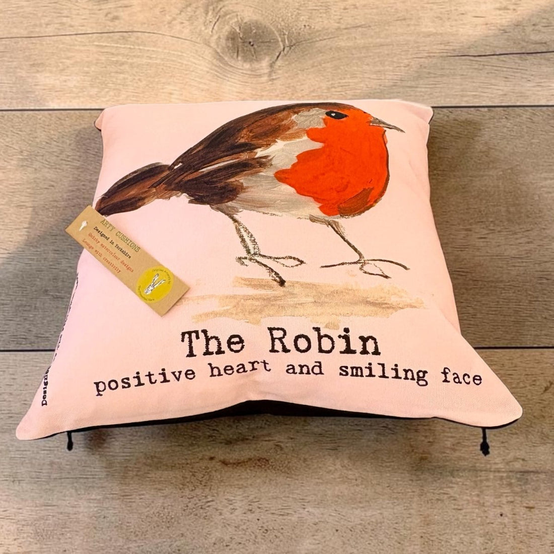 A square pink throw pillow featuring a painted robin bird and the text &