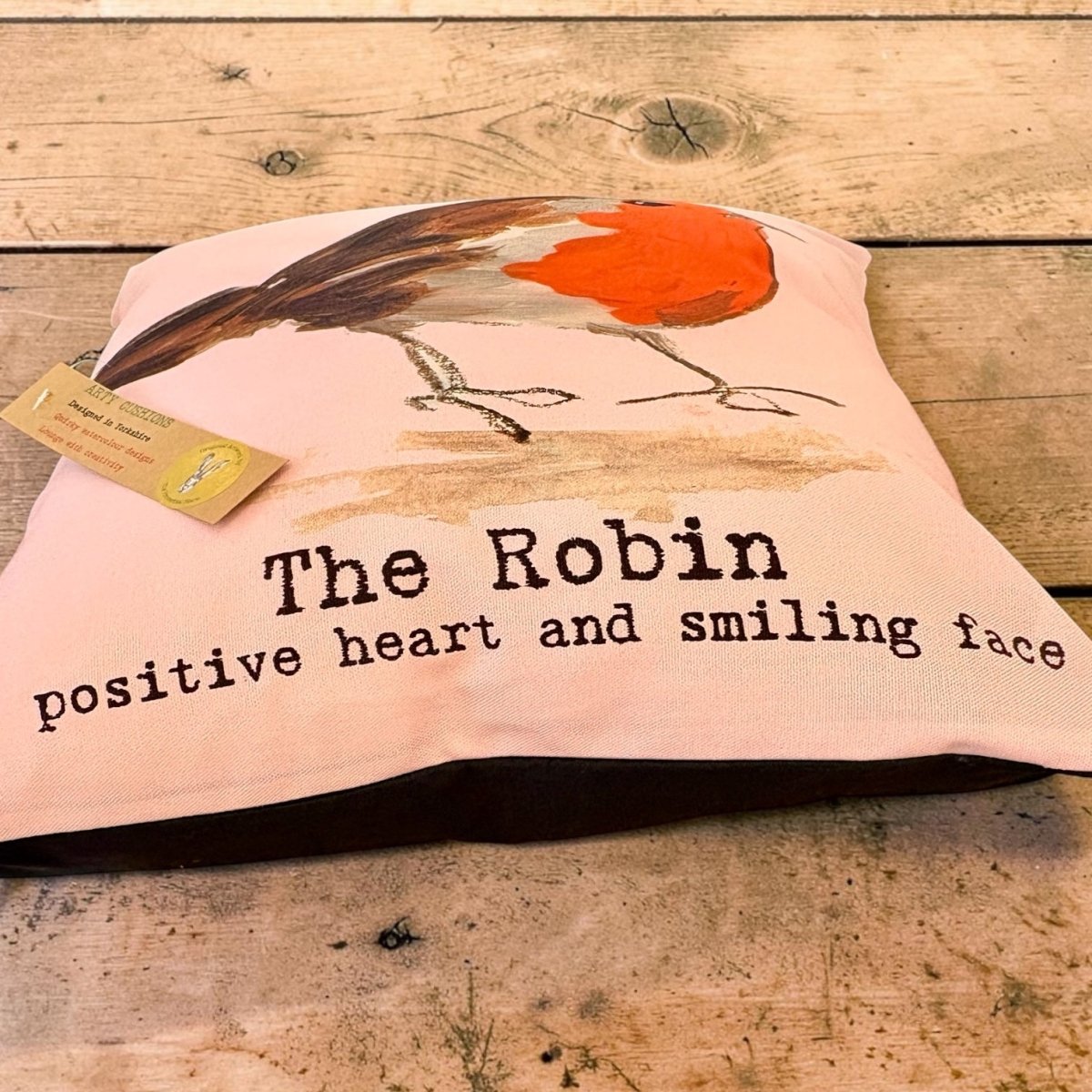 A square pink decorative pillow featuring a painted robin bird and the text &
