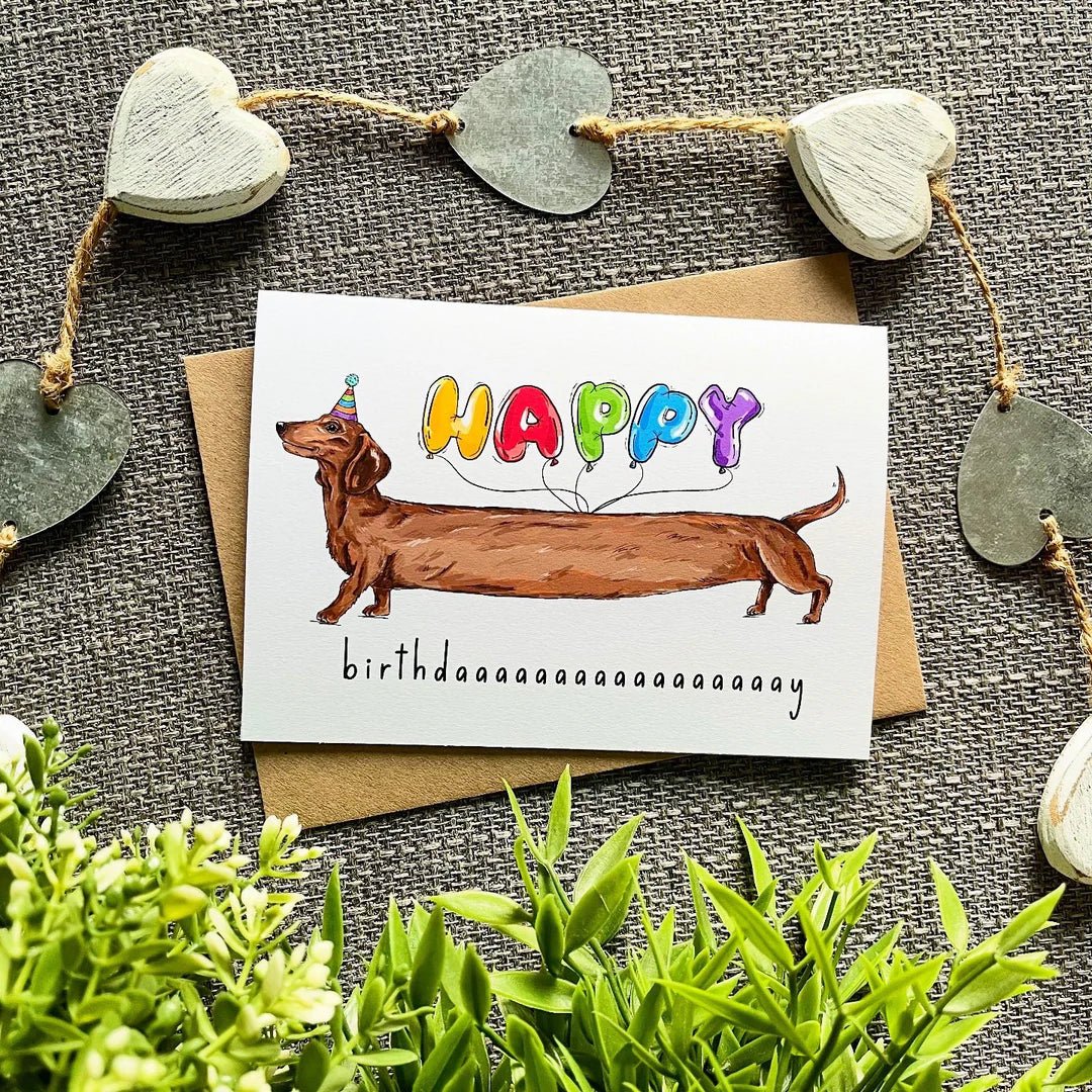 Birthday card with a dachshund and colorful balloons on a textured surface with heart decorations.