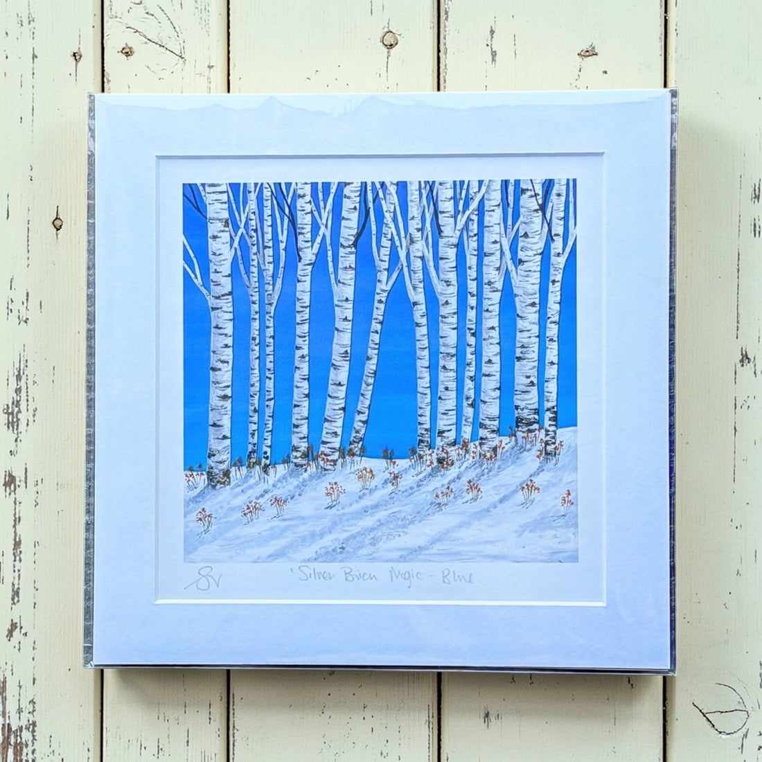 Framed artwork of birch trees against a blue sky on a wooden surface