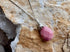 Pink teardrop pendant on a silver chain against a textured stone background