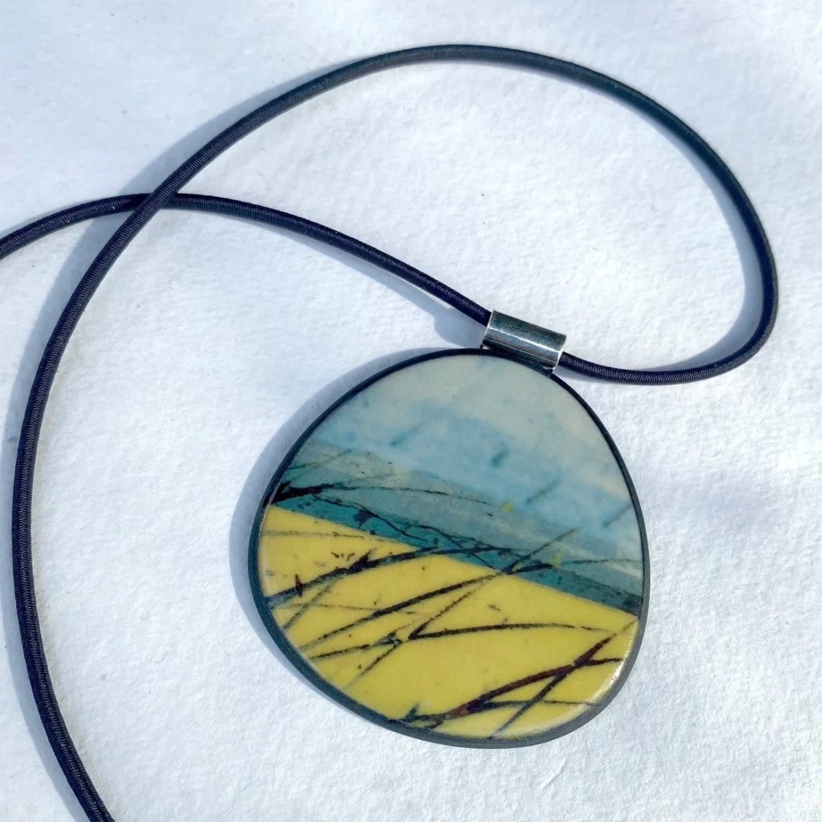 Round pendant with a blue and yellow design on a black cord against a white background