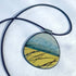 Round pendant with a blue and yellow design on a black cord against a white background