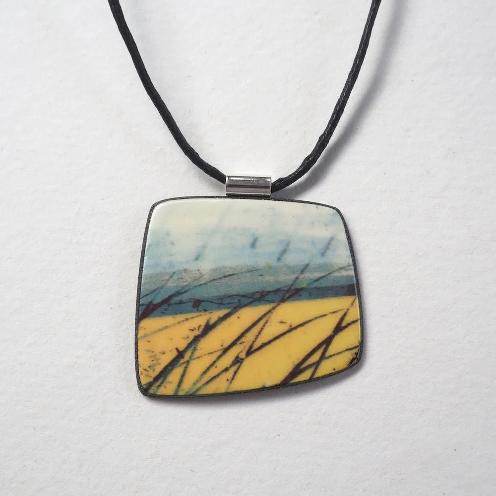 Square pendant with nature-themed design on a black cord against a white background