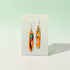 Orange earrings with floral design on a Nancy Jones card against a light green background