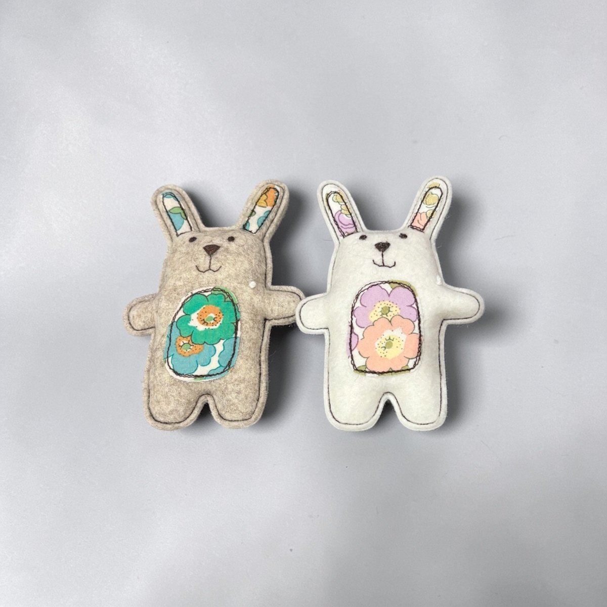 Two handmade rabbit toys with floral designs on a gray background