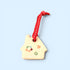 A small house-shaped ceramic ornament in a warm cream color, decorated with colorful painted flowers and a red heart, hanging from a red ribbon with white dots, set against a solid light blue background.