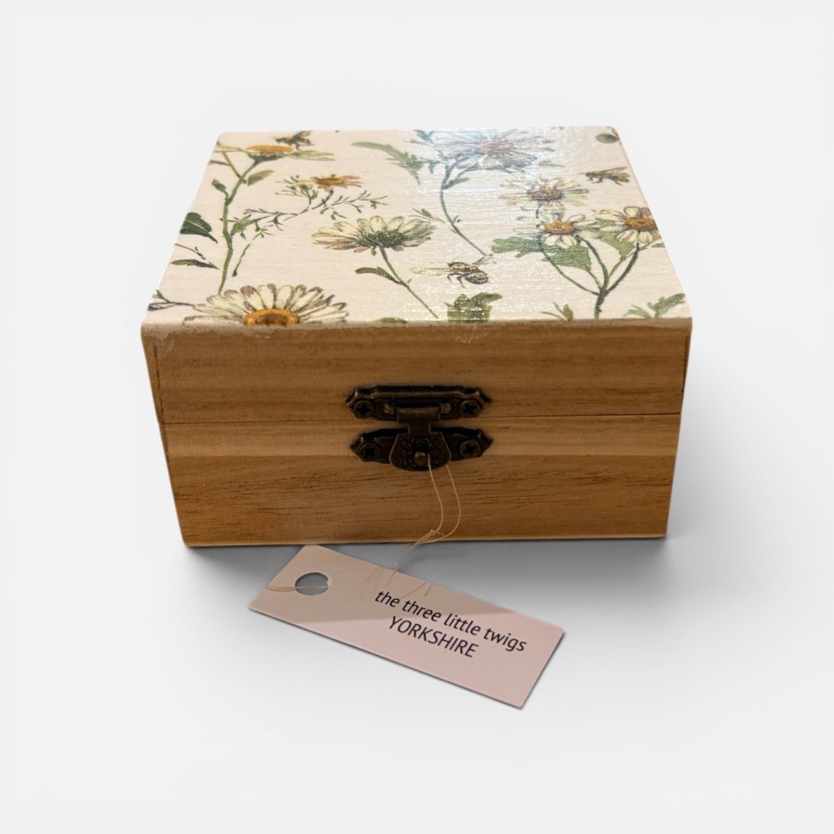 A square wooden keepsake box with a floral-patterned lid and a dark metal clasp, shown on a light gray background with a hanging tag that reads &