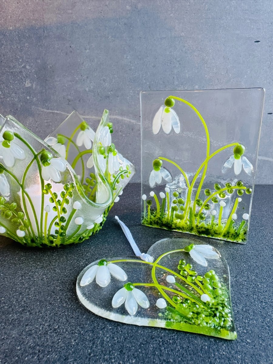 Transparent glass pieces with white snowdrop designs on a dark surface
