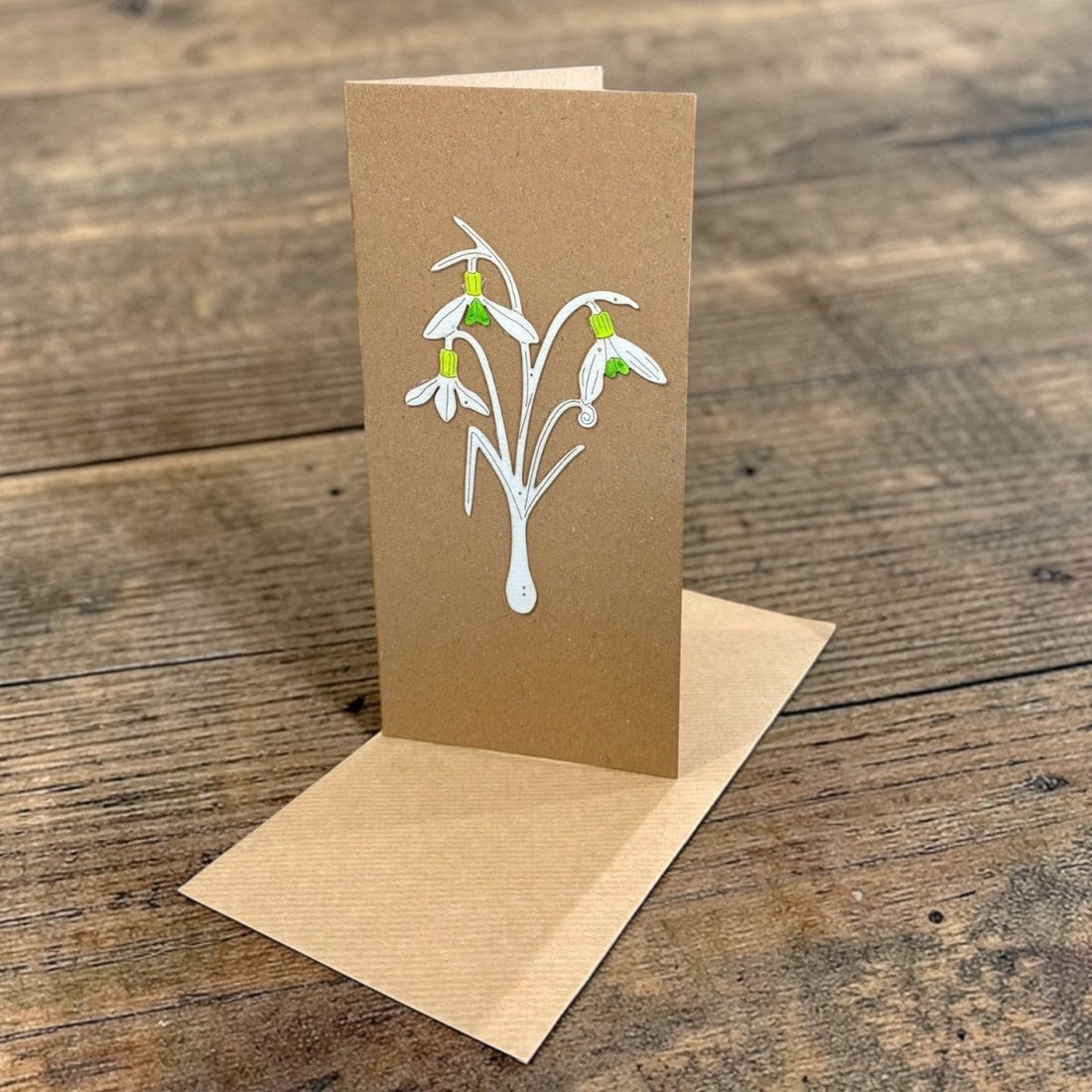 Kraft paper card with snowdrop design on a wooden surface