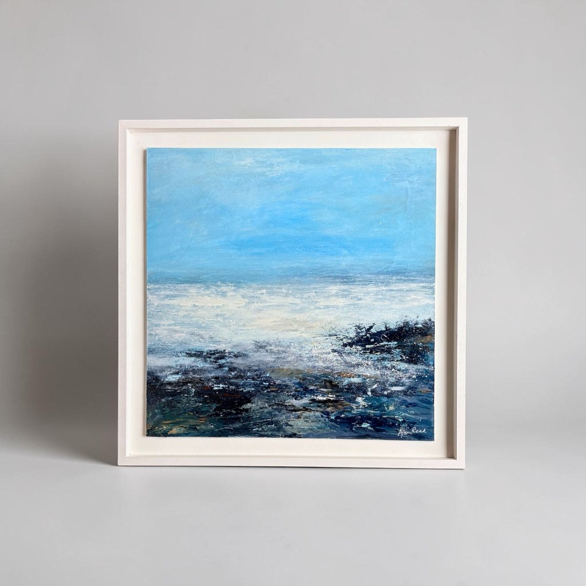 Framed painting of a coastal scene with blue sky and water.