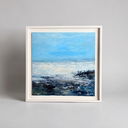Framed painting of a coastal scene with blue sky and water.