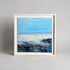 Framed painting of a coastal scene with blue sky and water.
