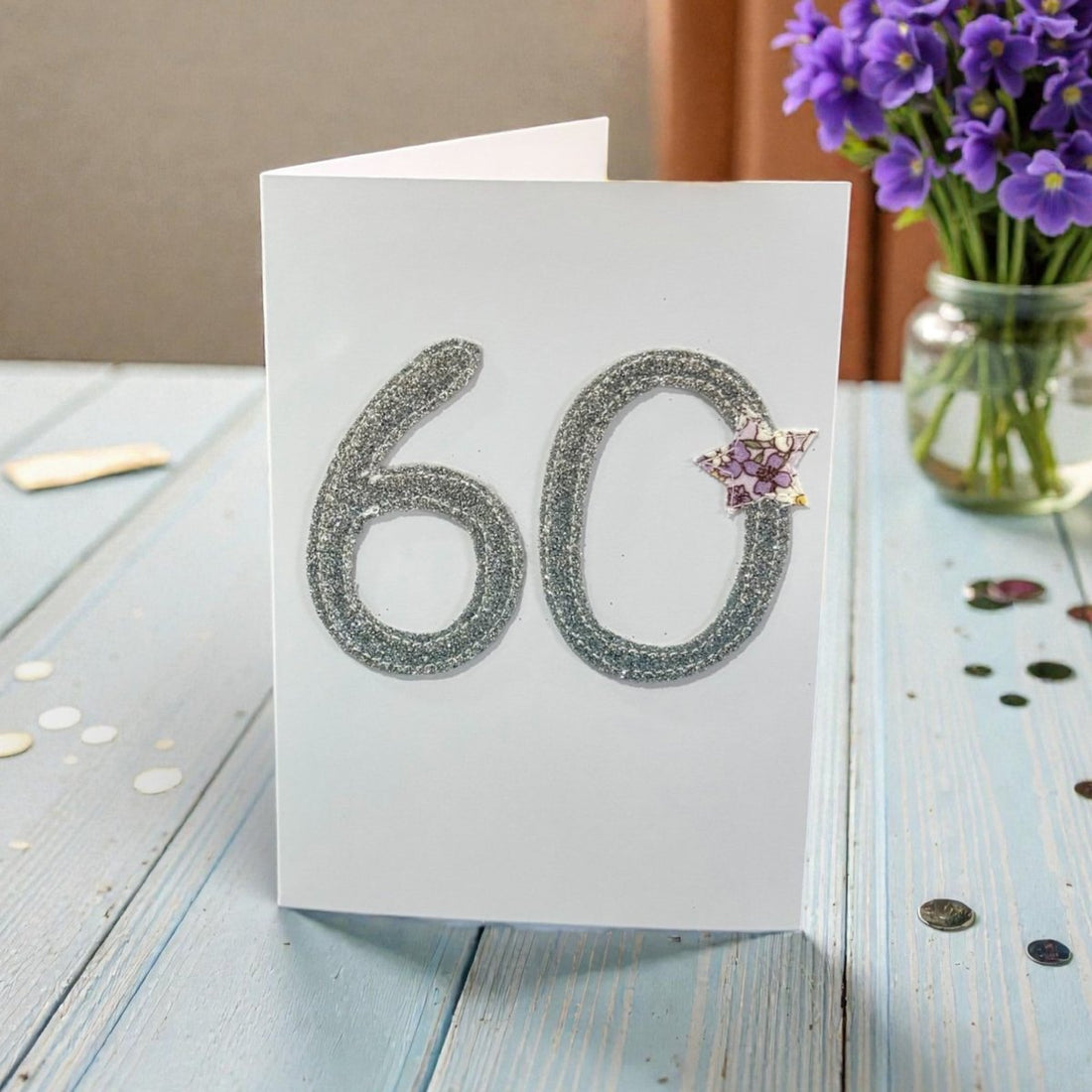 60th birthday card with glittery numbers on a wooden table with flowers in the background