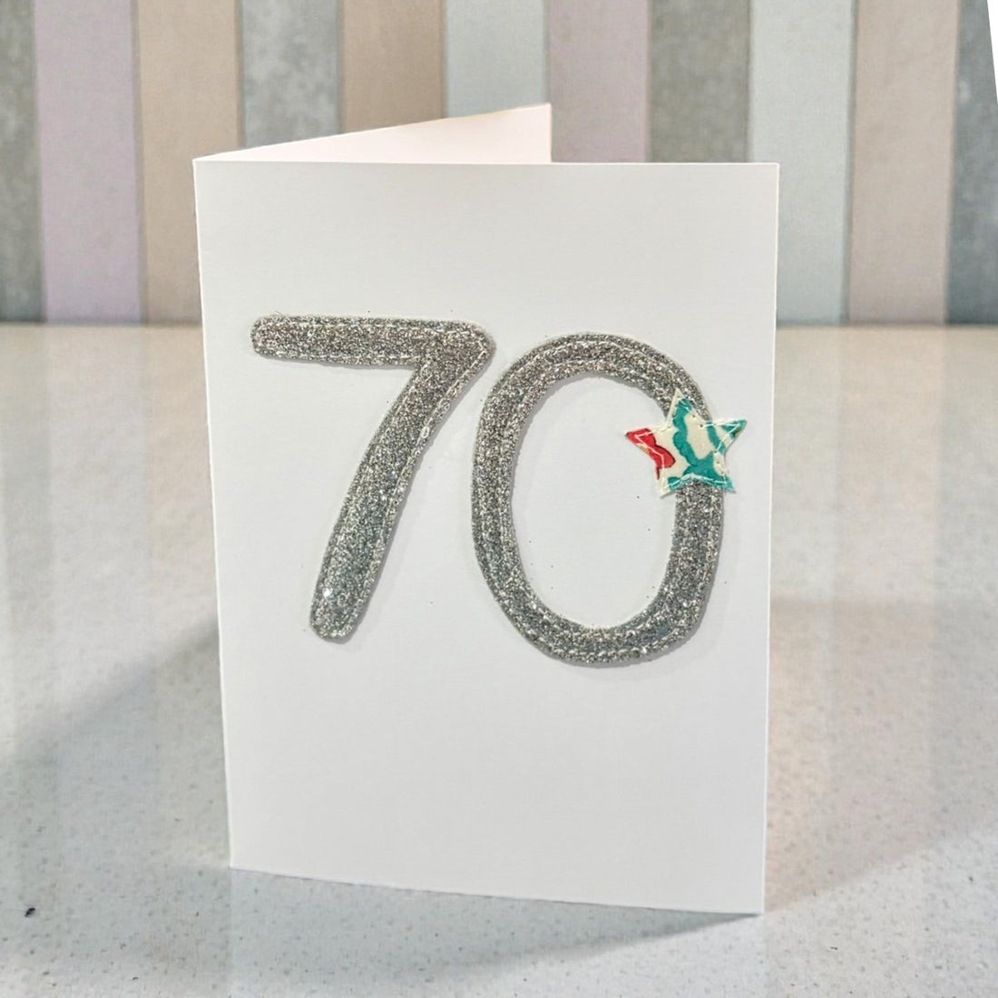 70th birthday card with glittery number 70 and a small green and red decoration on a striped background
