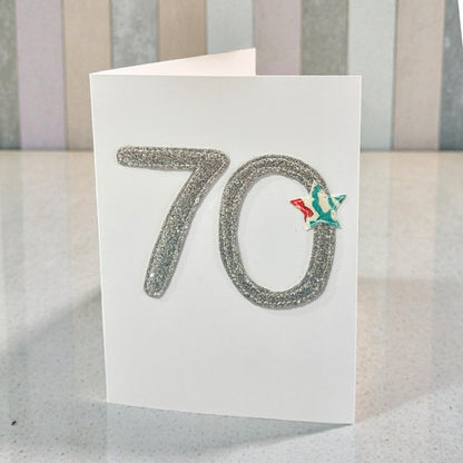 70th birthday card with glittery number 70 and a small green and red decoration on a striped background
