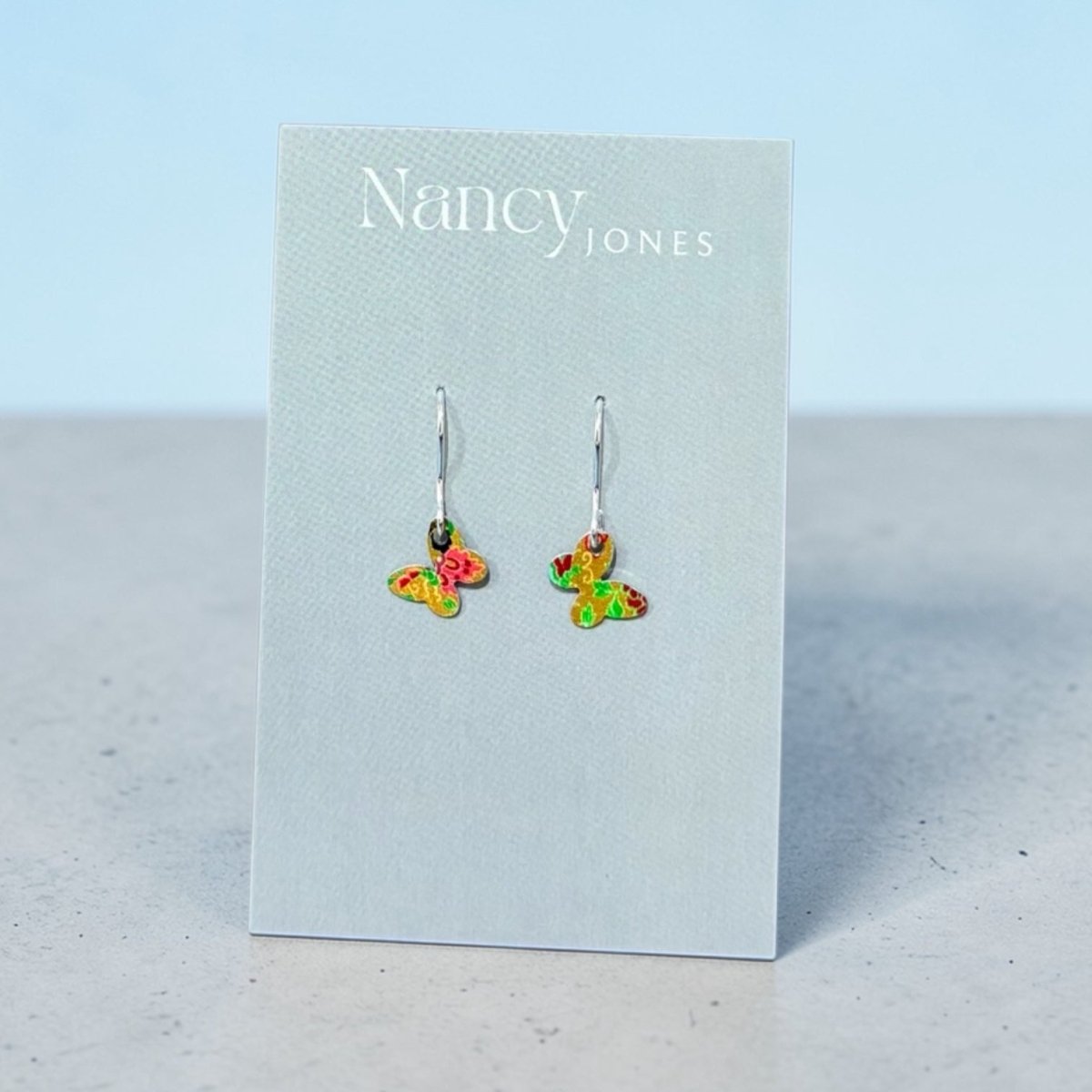 Butterfly-shaped earrings on a Nancy Jones card against a light blue background
