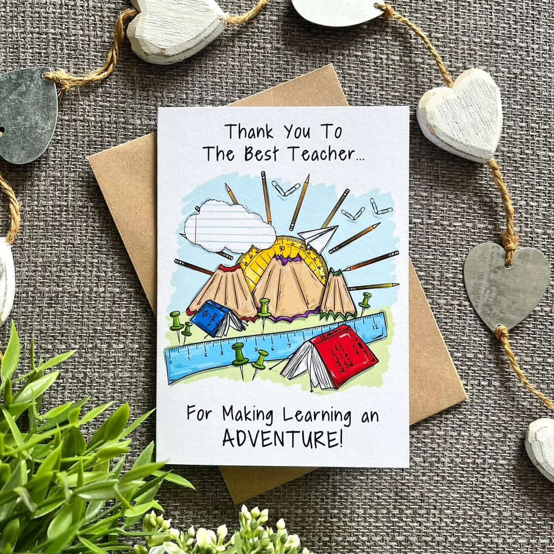 Card with teacher appreciation message and illustrations on a textured surface with decorative elements.