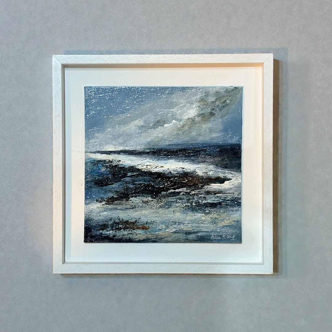 Framed artwork of a coastal scene with a white border on a gray wall.