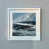Framed artwork of a coastal scene with a white border on a gray wall.