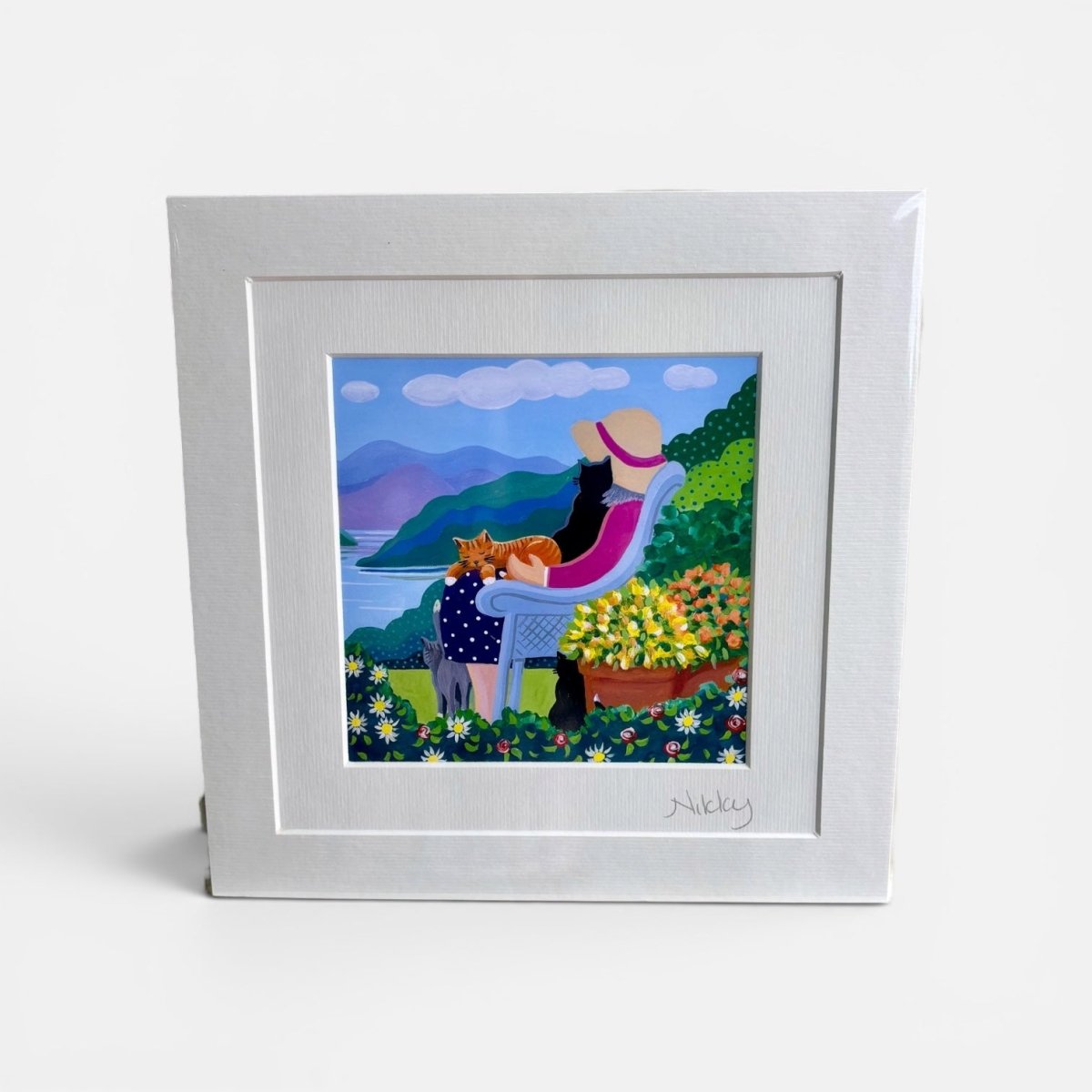 Framed artwork of a woman with a dog and cat sitting in a garden with mountains in the background.
