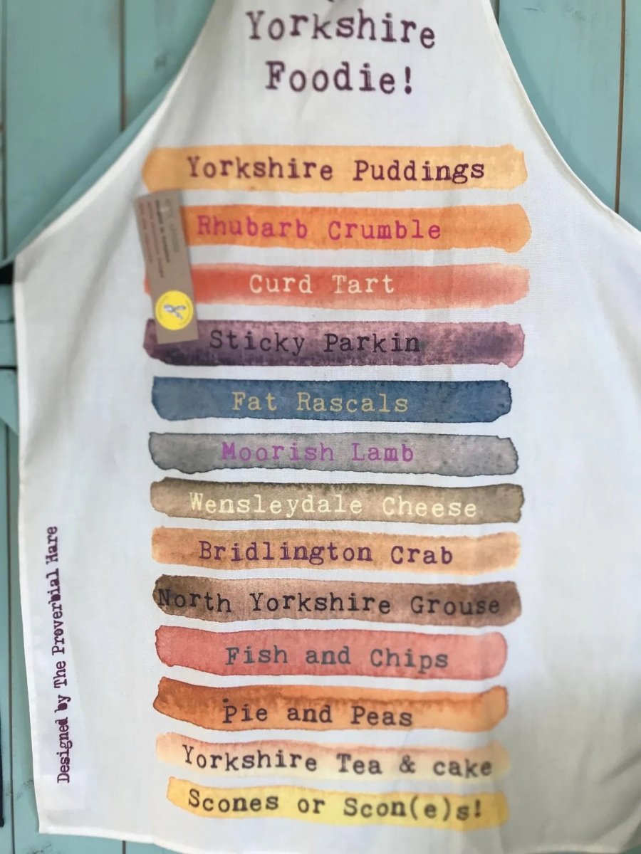 White apron with colorful text listing Yorkshire food items on a light blue background