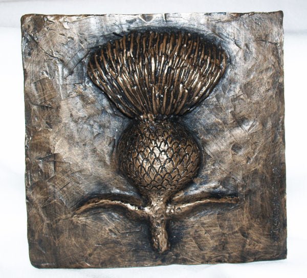 A square bronze wall plaque featuring a raised thistle design with textured metallic surfaces and a rustic finish, photographed against a plain white background.