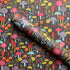 A roll of patterned wallpaper or fabric featuring a dense, whimsical mushroom design on a dark charcoal background. The pattern includes mushrooms in red, orange, yellow, purple, and light blue, with some featuring white polka dots.