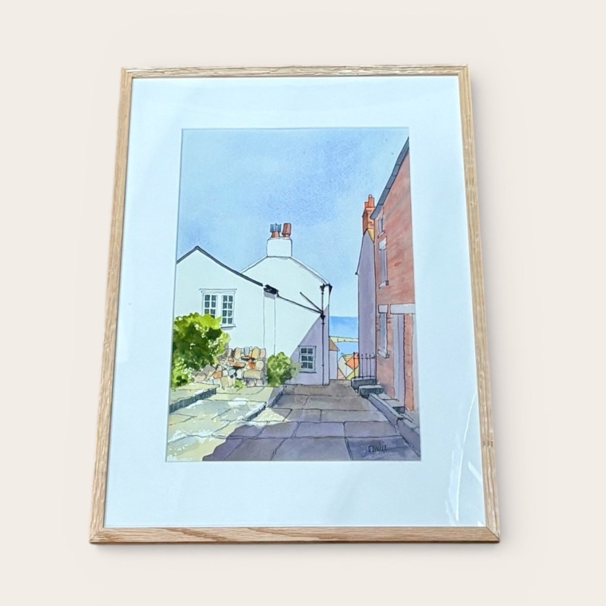 Framed artwork of a street scene with houses and people on a light blue background