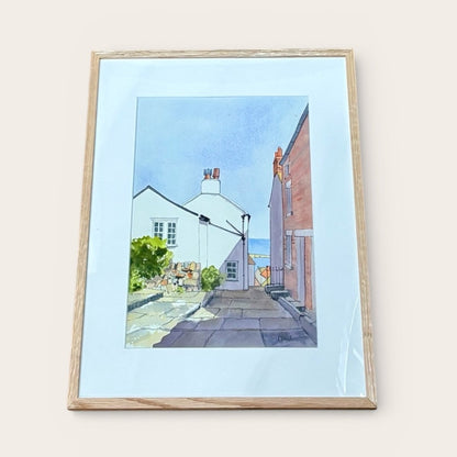 Framed artwork of a street scene with houses and people on a light blue background