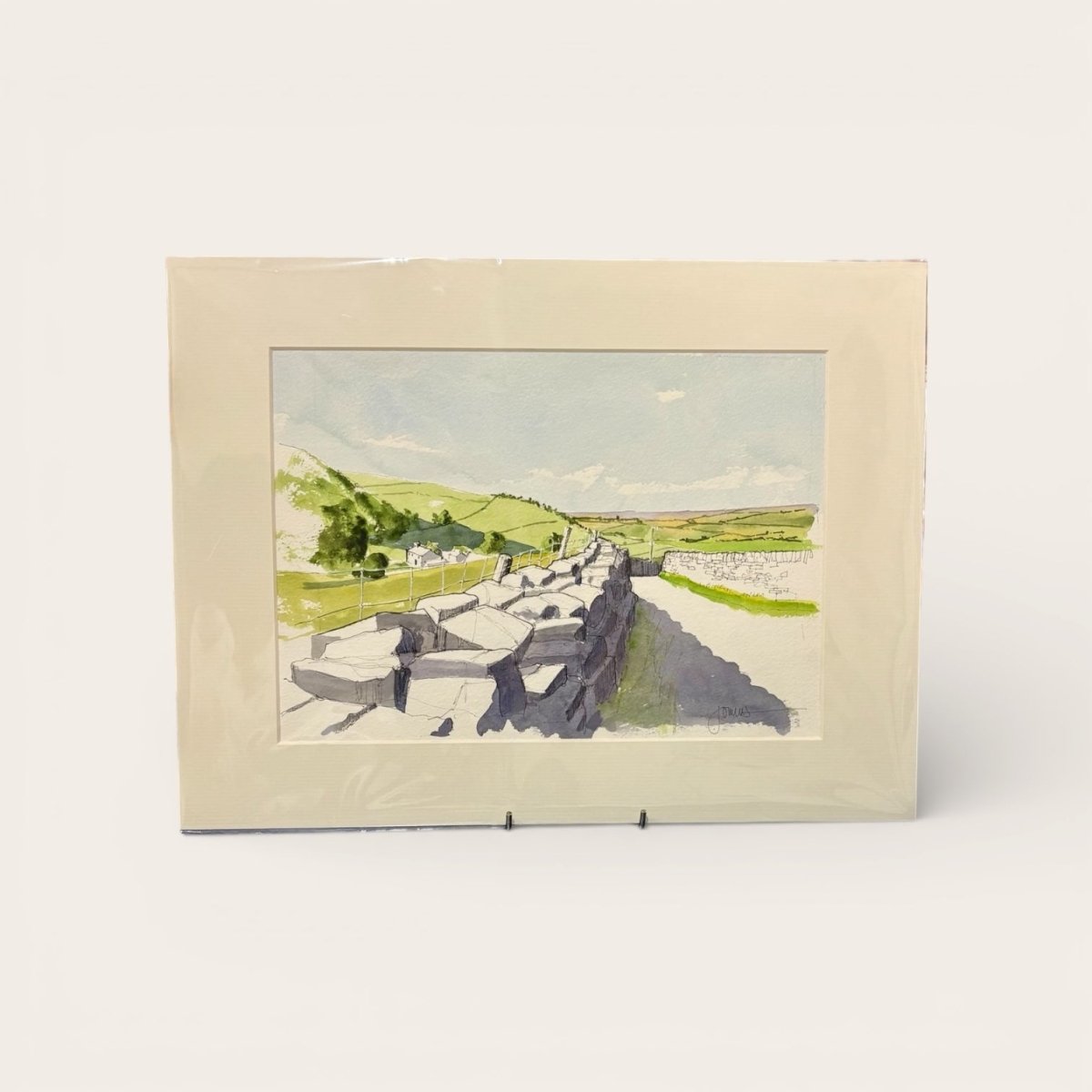 Framed watercolor landscape painting of a stone wall and green fields.