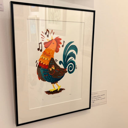 A framed black and white art print featuring a whimsical sheep illustration, displayed on a white gallery wall with a small label card visible at the bottom left.