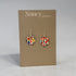 A pair of Nancy Jones floral enamel flower-shaped drop earrings displayed on a brown cardboard brand card against a neutral gray background.