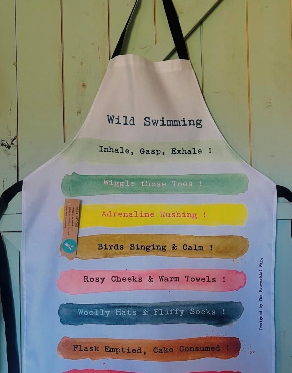 Colorful apron with text about wild swimming hanging against a wooden wall.