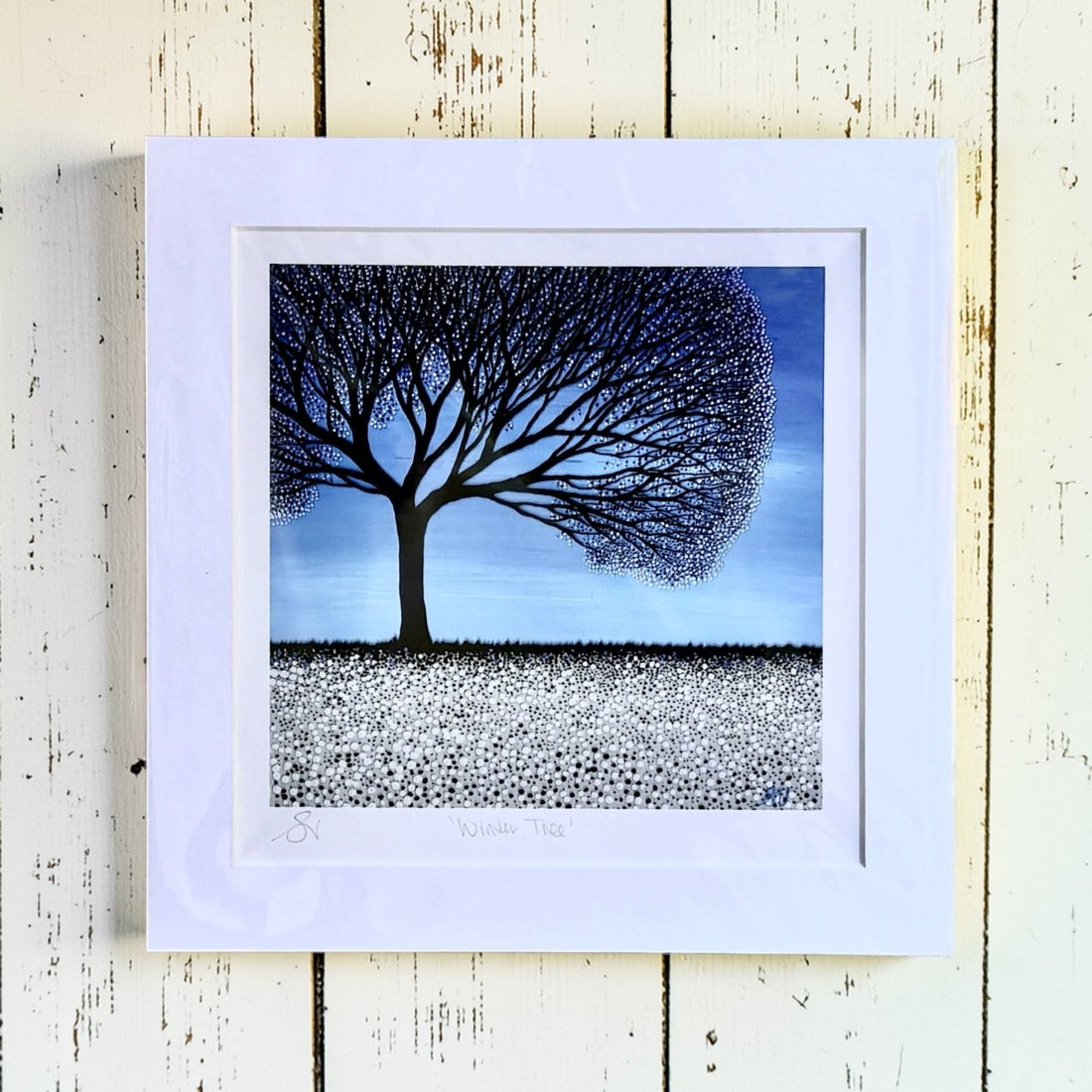 Framed artwork of a tree with a blue sky background on a wooden surface