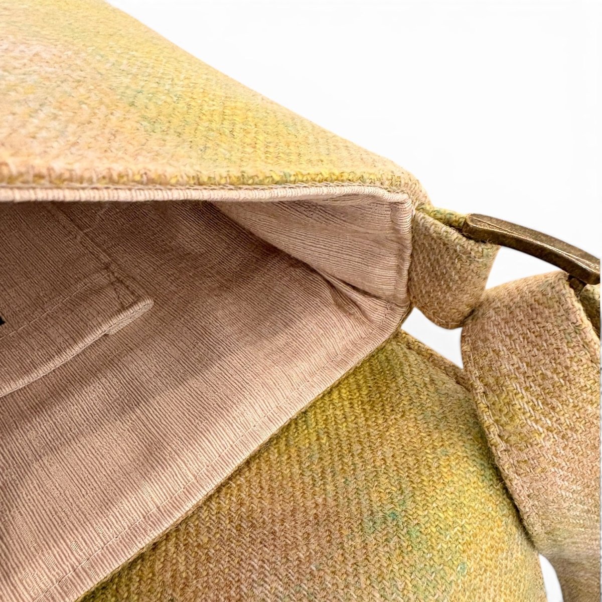 Close-up of a textured woven shoulder bag in a muted yellow-green and beige color, showing the interior lining and a portion of the strap with a metal ring.