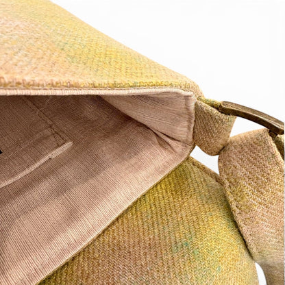 Close-up of a textured woven shoulder bag in a muted yellow-green and beige color, showing the interior lining and a portion of the strap with a metal ring.