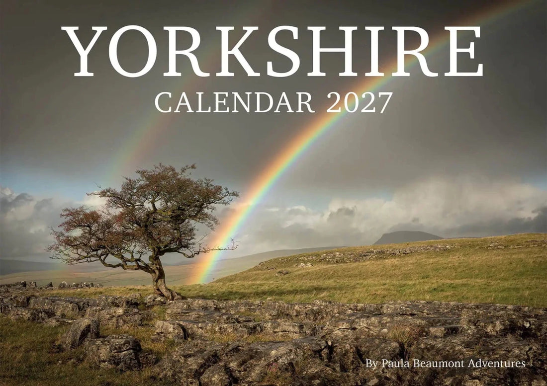Yorkshire Calendar 2027 cover featuring a dramatic landscape photograph of a lone tree under a cloudy sky with a rainbow arching over green hills. Large white text at the top reads &