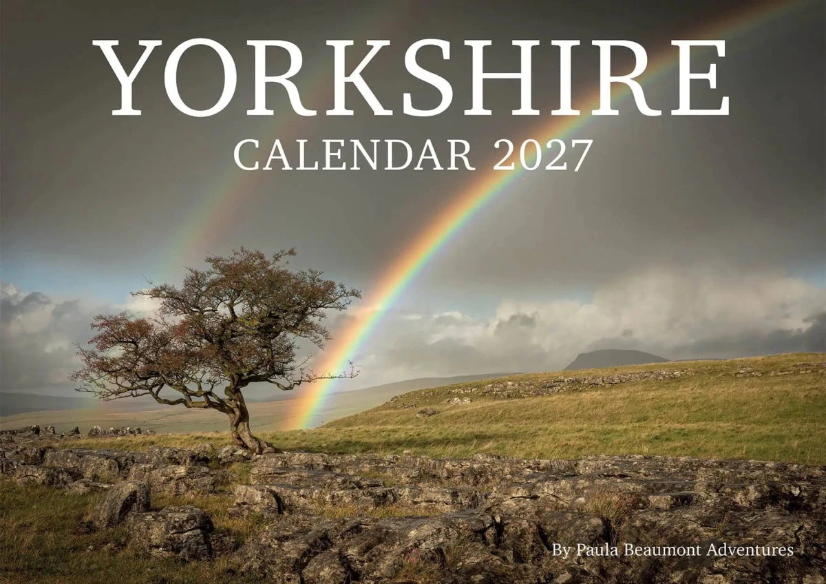 Yorkshire Calendar 2027 cover featuring a dramatic landscape photograph of a lone tree under a cloudy sky with a rainbow arching over green hills. Large white text at the top reads &